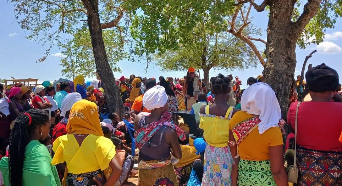 Multidão de mulheres debaixo de árvores, vistas de costas, durante uma distribuição de kits de dignidade