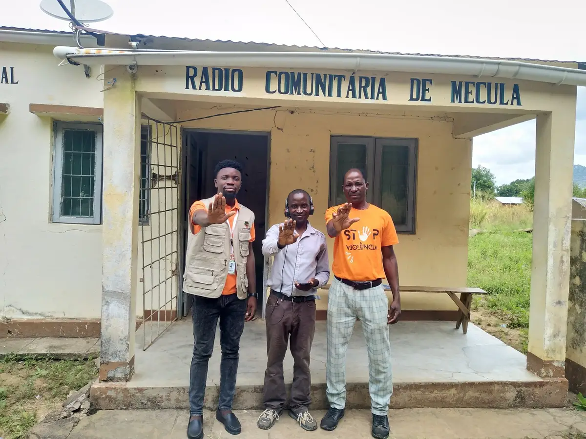 Membro da equipa da GCR e dois técnicos da rádio fazem o gesto de «basta» em frente à Rádio Comunitária de Mecula