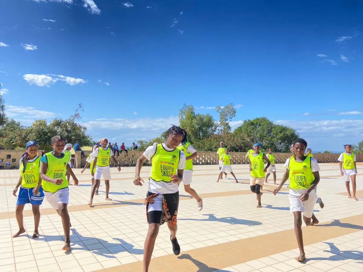 Raparigas com coletes da Equipa SKILLZ correm num campo de jogos