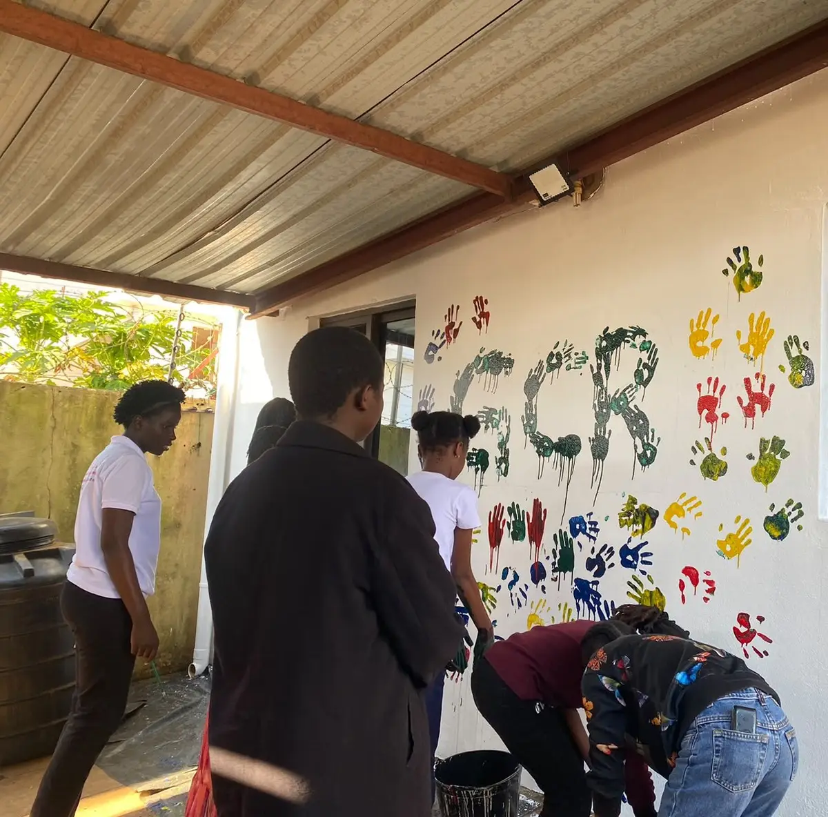 Pessoas, de costas, imprimem as mãos numa parede com as letras GCR