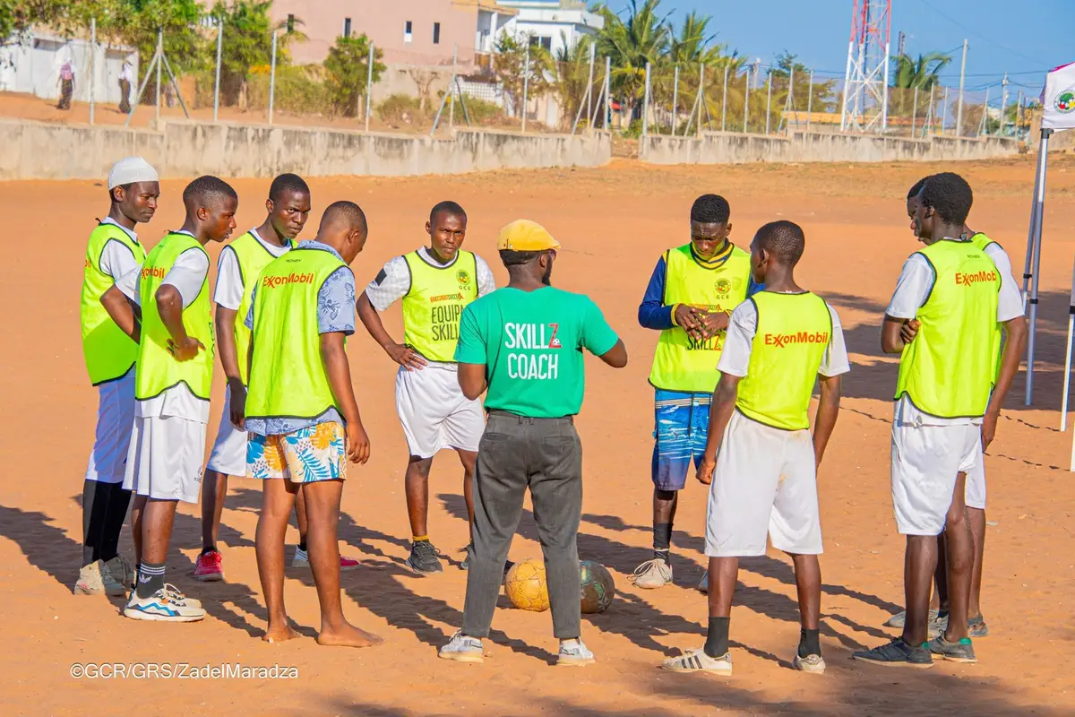 Treinador do programa SKILLZ dá instruções a jovens jogadores num campo de areia