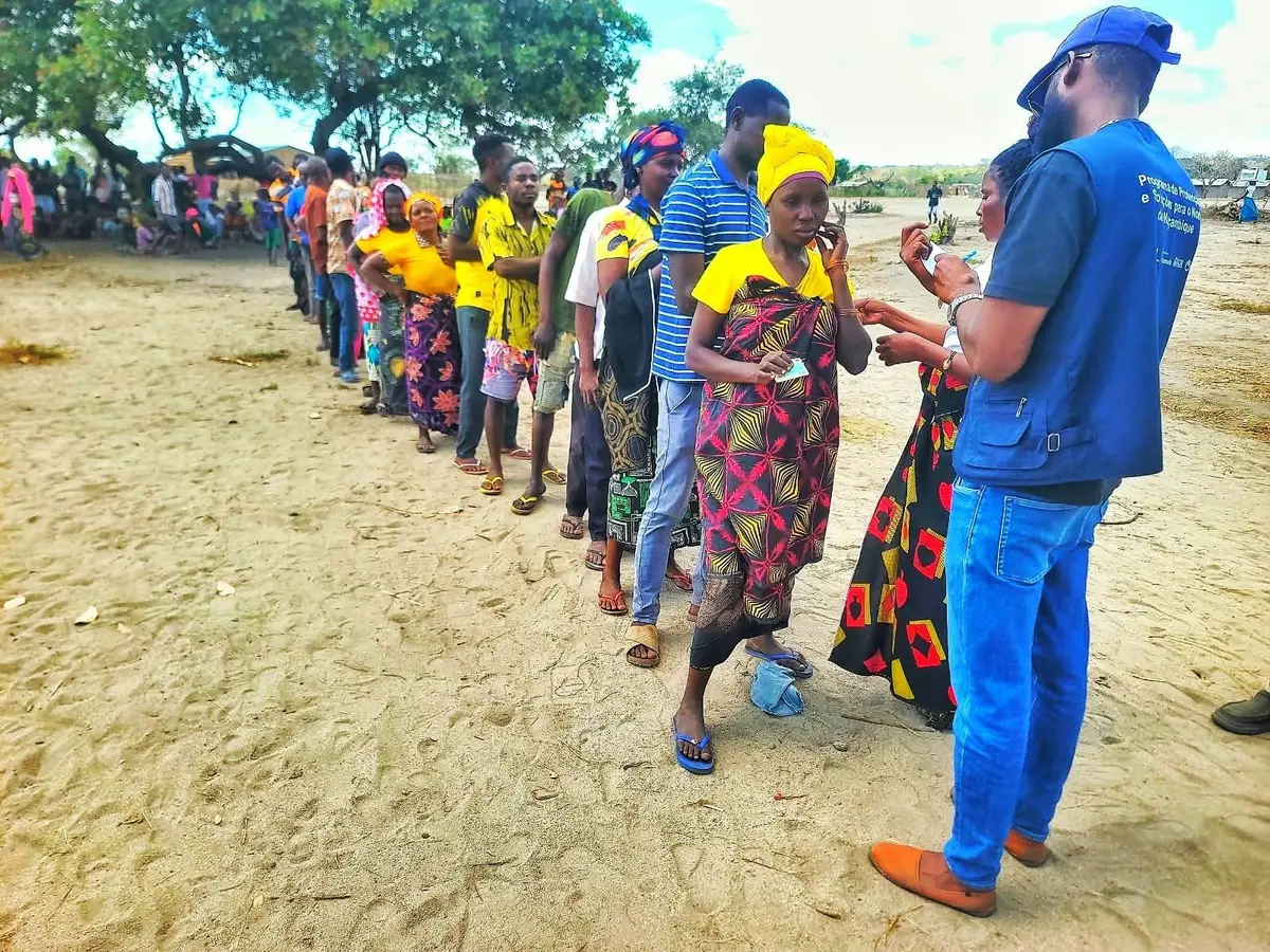 Membro da equipa do consórcio, de colete, verifica uma fila de mulheres durante a distribuição